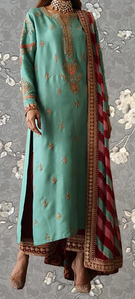 A woman wearing a long, green dress with gold embroidery and a red and gold shawl draped over her shoulders.