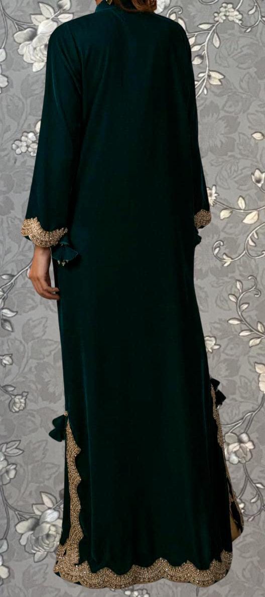 A person wearing a long, dark green dress with gold trim, standing against a floral background.