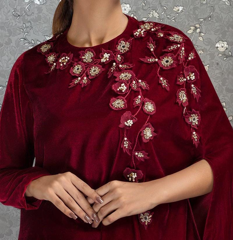 A close-up of a person wearing a burgundy dress with intricate floral embroidery on the neckline and sleeves.