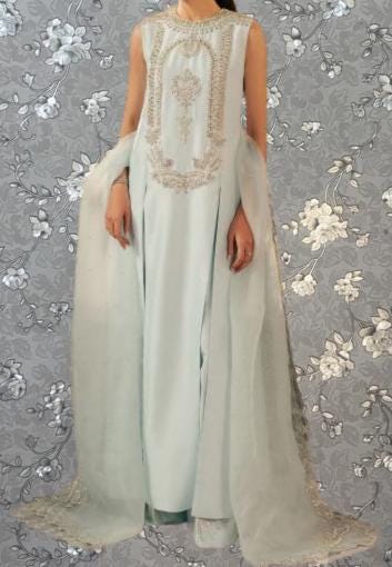 A woman wearing a long, light blue dress with a beaded bodice and a flowing, draped skirt.
