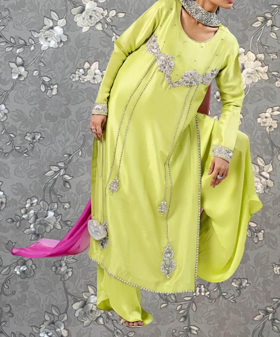 A person wearing a bright yellow dress with intricate beading and embroidery, posing against a gray floral background.
