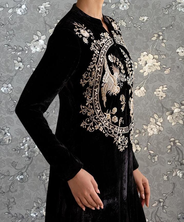 A person wearing a black velvet dress with intricate gold embroidery on the front.