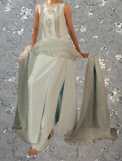 A woman wearing a white dress with a long train and a gray shawl is standing against a gray floral background.
