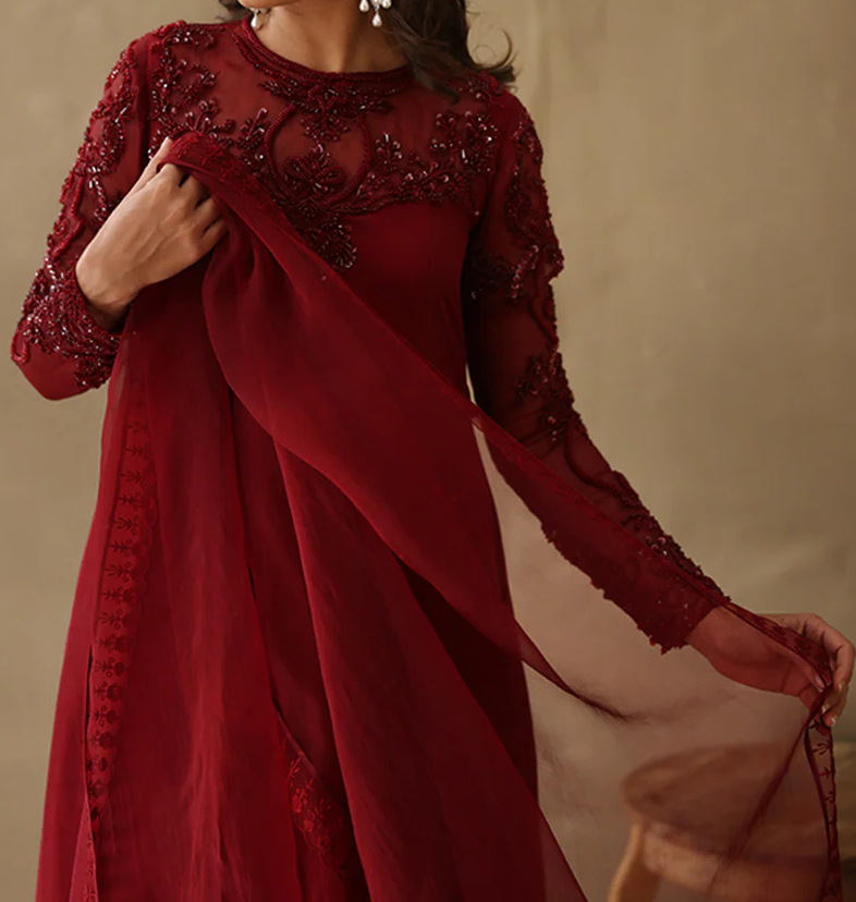 A woman wearing a red dress with intricate embroidery and a flowing, sheer fabric draped over her.