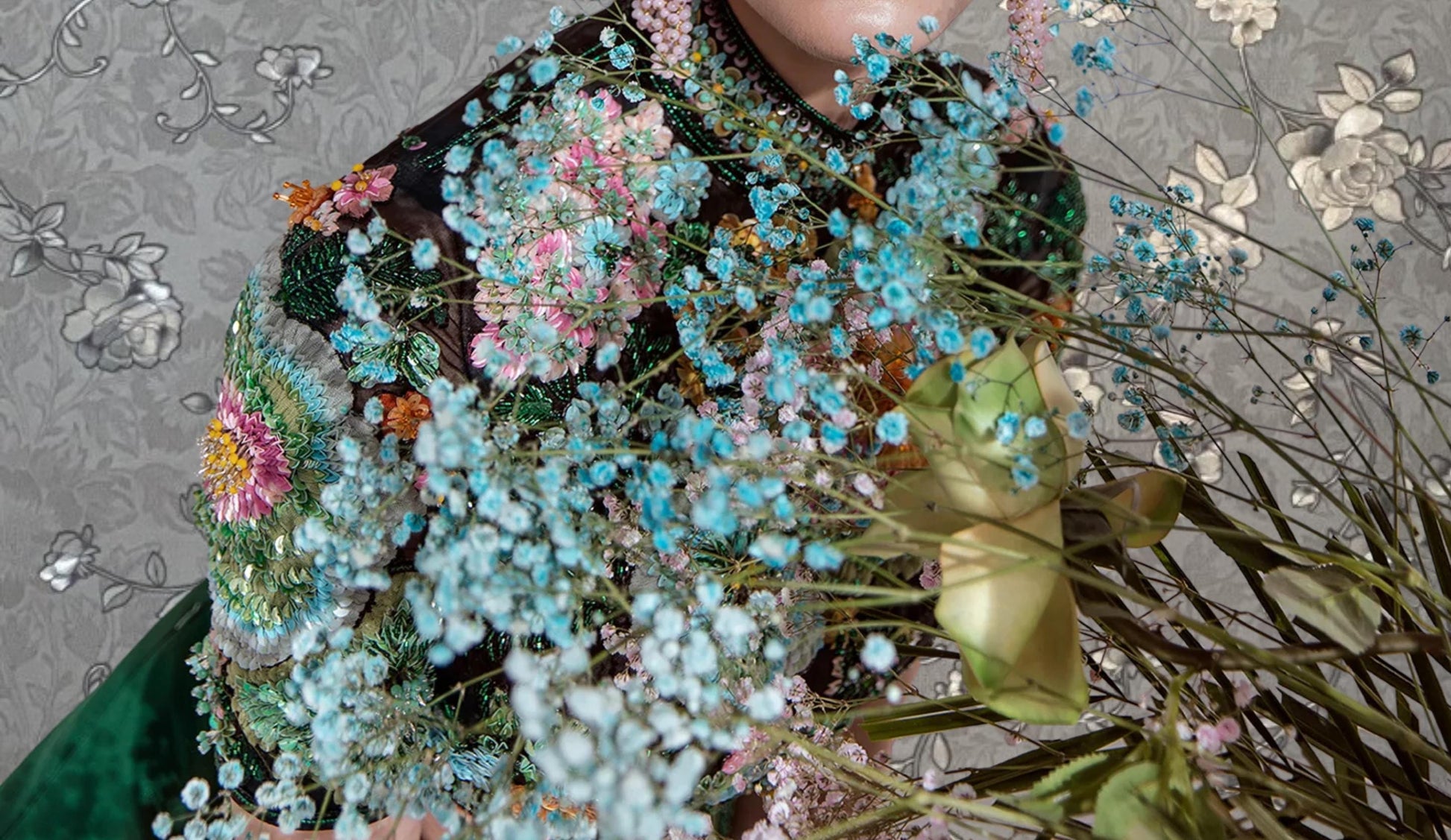 a person wearing a black jacket with a floral pattern, surrounded by a variety of colorful flowers and plants.