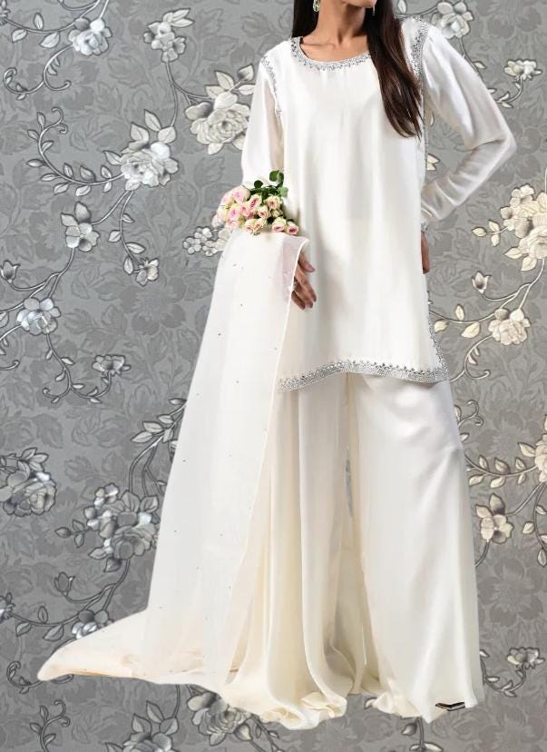 A woman wearing a white dress with a long train and holding a bouquet of flowers stands against a gray floral background.