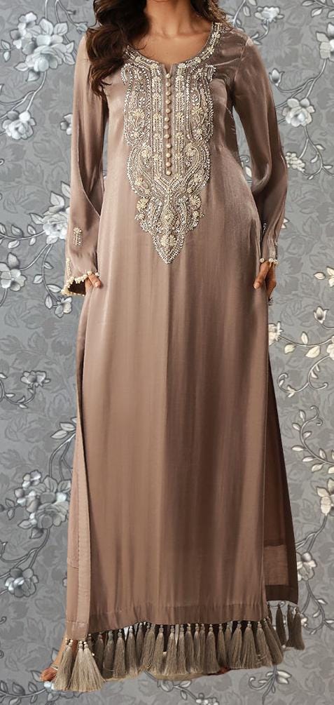 A woman wearing a long, beige dress with intricate embroidery and tassels on the bottom.