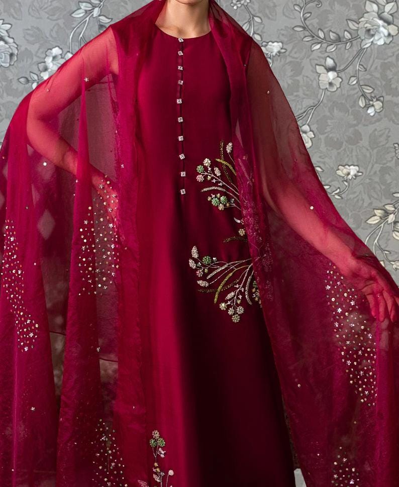 A woman wearing a red dress with a sheer, embroidered shawl draped over her shoulders.