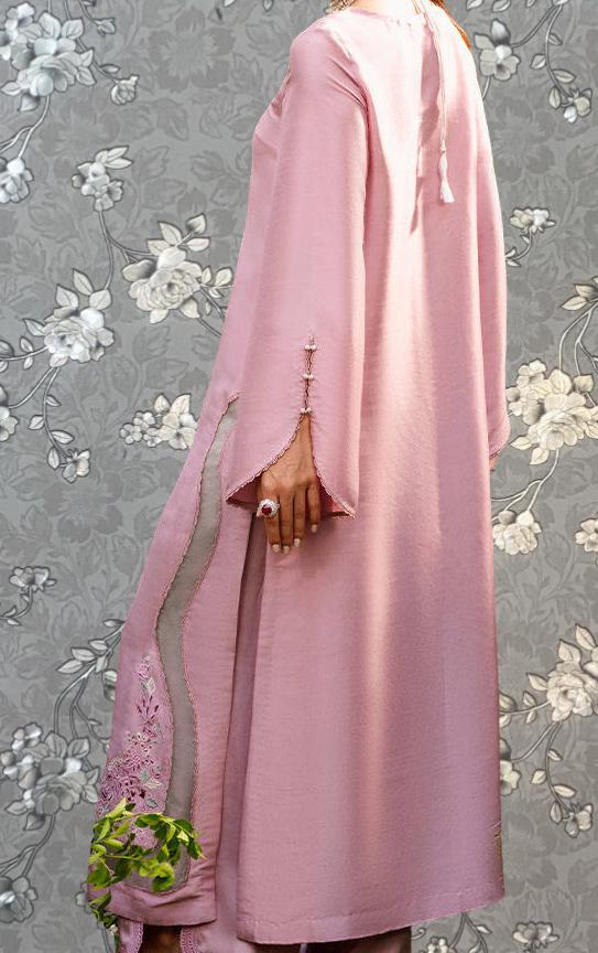 A person wearing a long pink dress with a floral pattern and holding a small green plant.