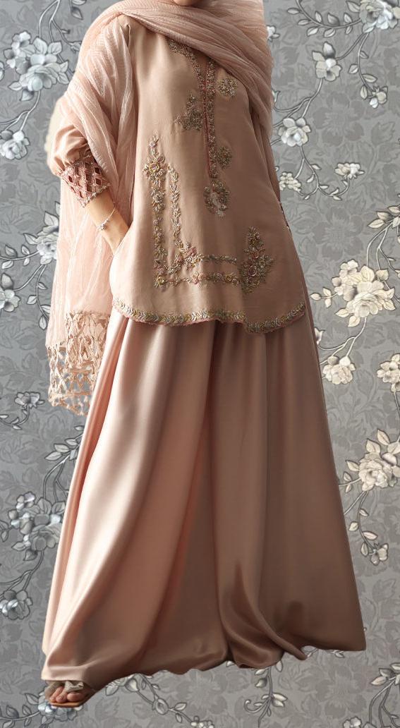 A woman wearing a long, peach-colored dress with intricate embroidery and a matching shawl.