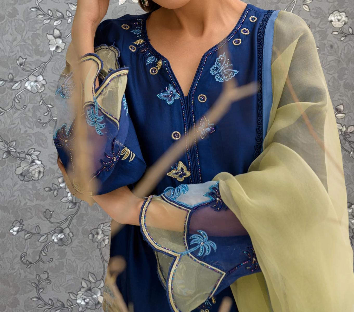 A close-up of a woman wearing a blue dress with intricate embroidery and a yellow shawl draped over her shoulders.