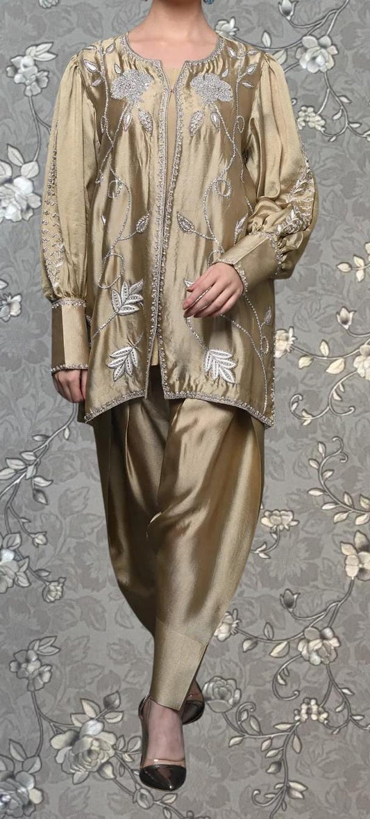 A person wearing a gold-colored dress with intricate embroidery and floral patterns, standing against a gray floral background.