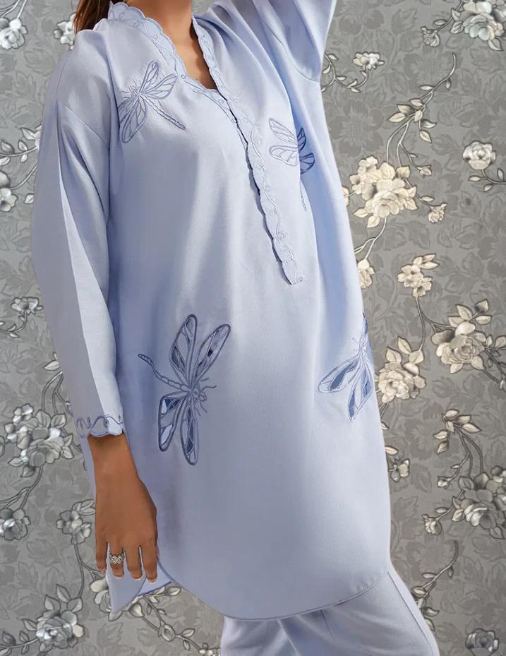A woman wearing a light blue dress with blue butterfly designs on it, standing against a gray floral background.