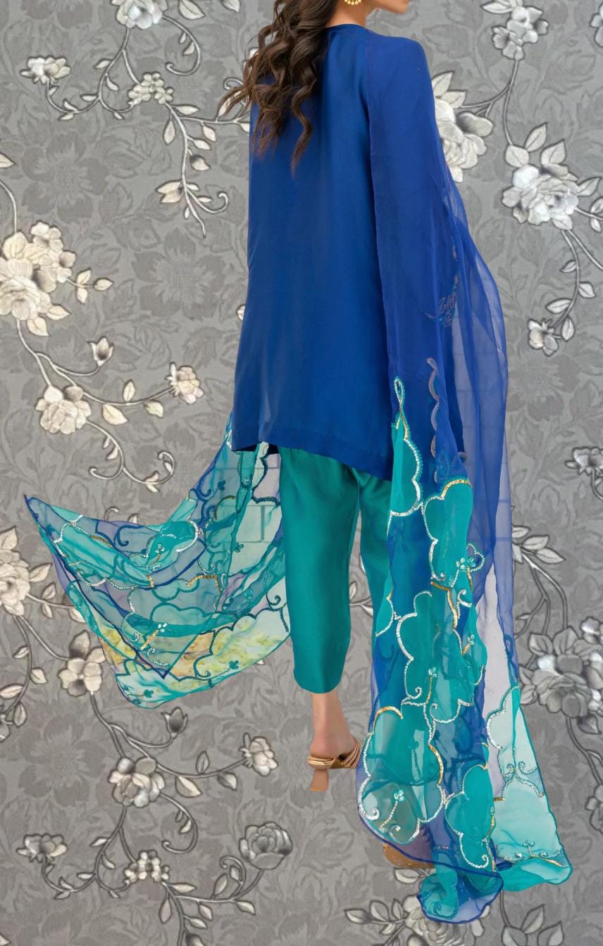 A woman wearing a blue blouse and green pants with a long, flowing blue and green patterned shawl.