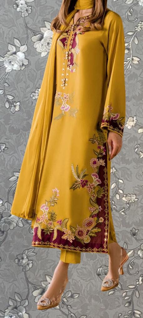 A woman wearing a yellow dress with intricate floral embroidery, standing against a gray floral background.