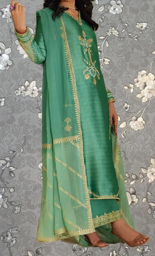 A woman wearing a long, green dress with gold embroidery and a matching green shawl.