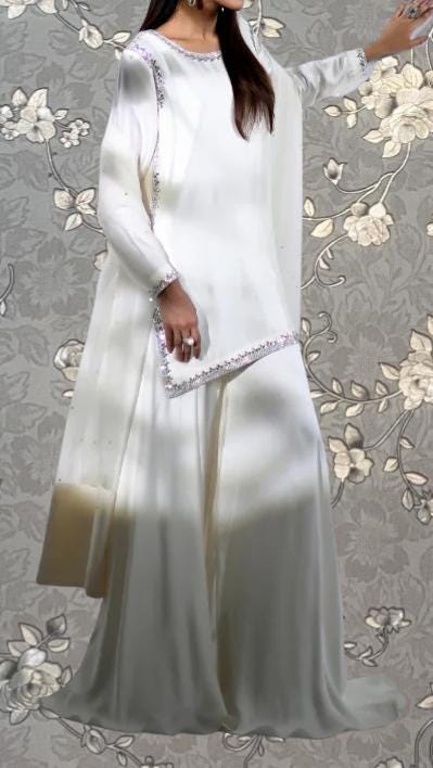 A woman wearing a long white dress with a floral pattern on the skirt and a matching white blouse.