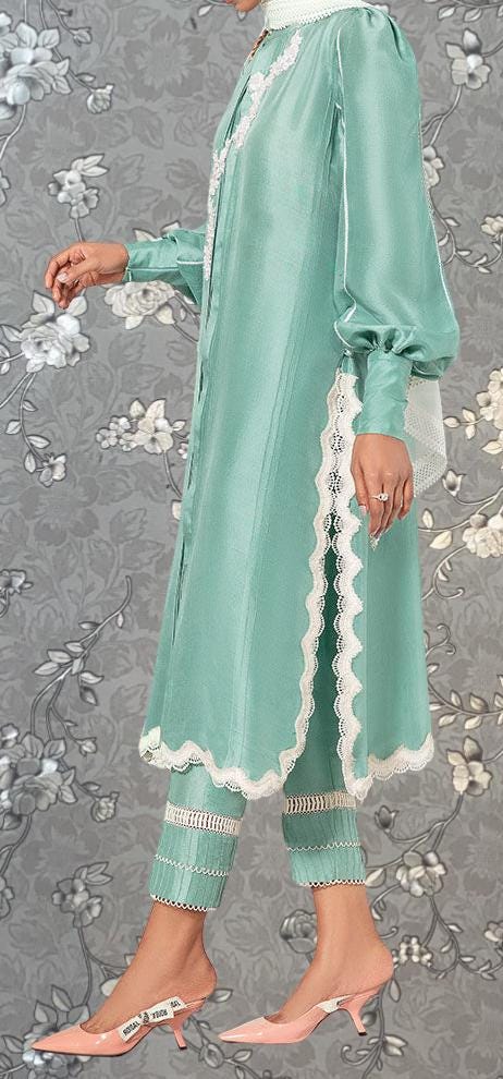A person wearing a mint green dress with lace trim and high heels stands against a gray floral background.
