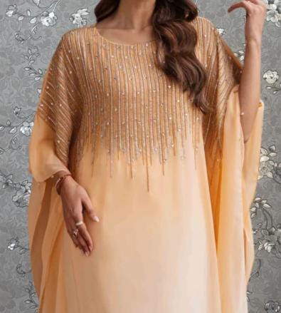 A woman wearing a peach-colored dress with a gold and silver embellished design, posing against a gray floral background.