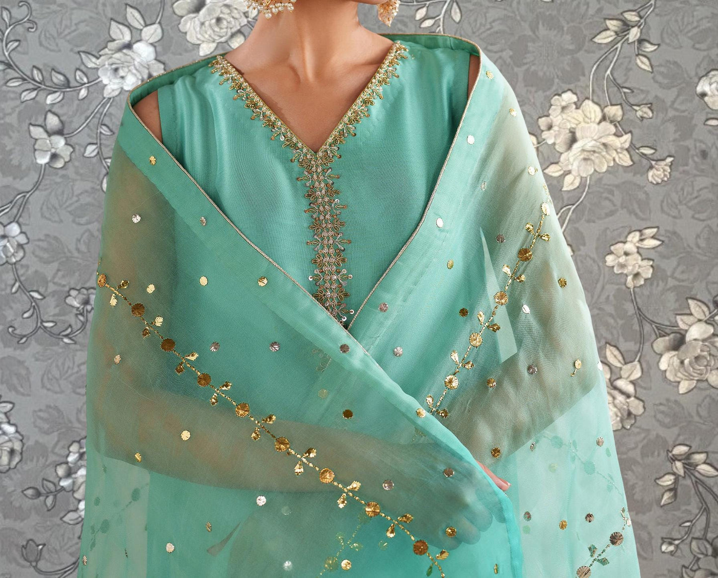 A close-up of a person wearing a turquoise dress with gold embroidery and a sheer green shawl with gold sequins.