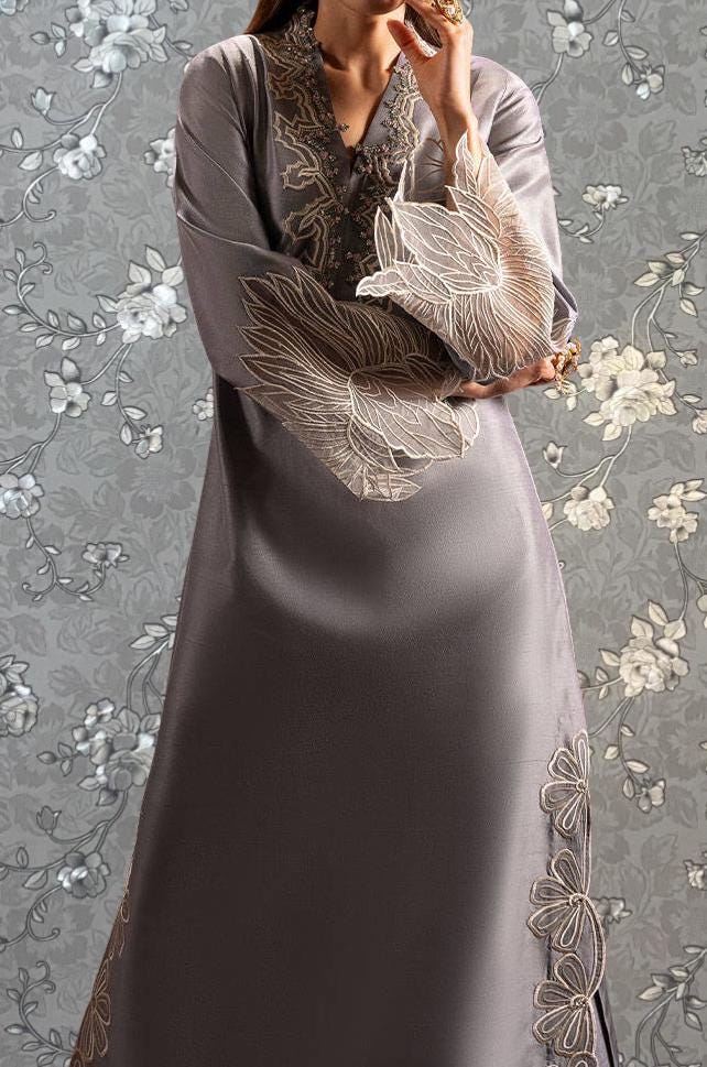 A woman wearing a long gray dress with intricate embroidered designs on the sleeves and hem.