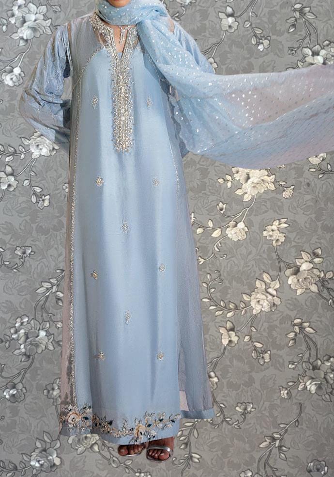 A woman wearing a long, light blue dress with intricate embroidery and a matching light blue scarf.