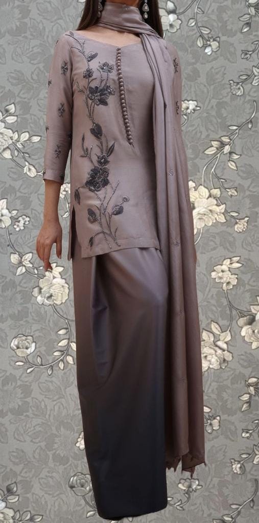 A woman wearing a long, gray dress with floral embroidery on the front.