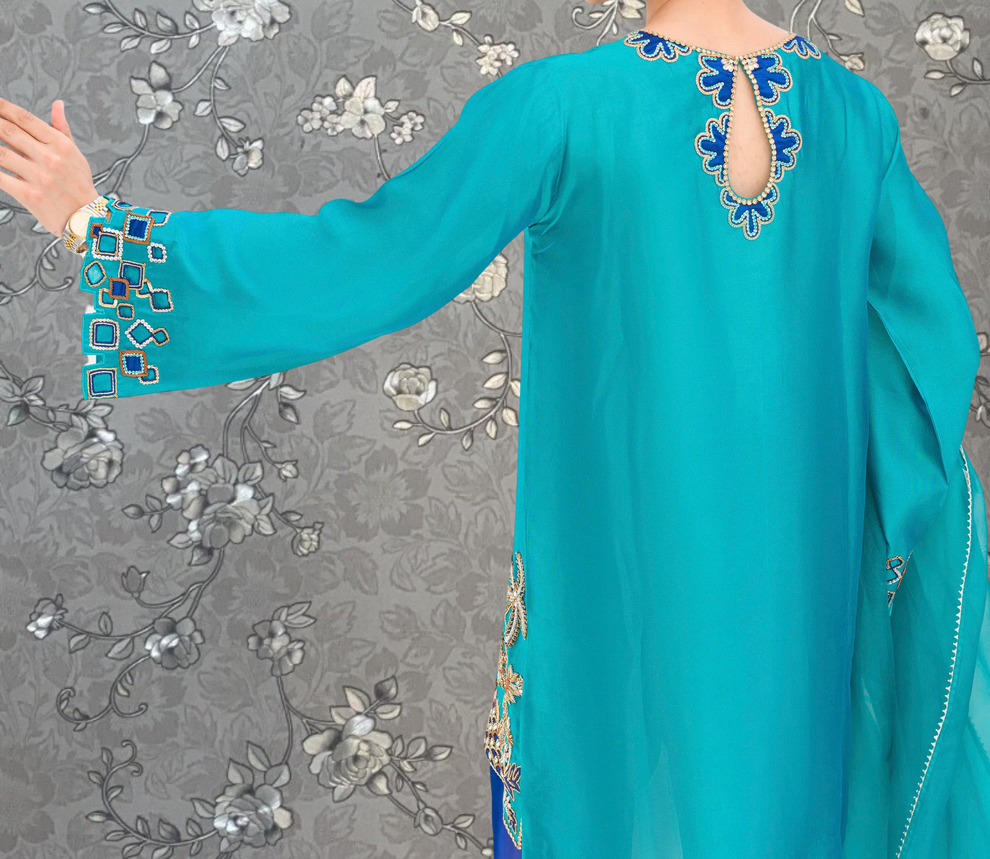 A close-up view of a person wearing a turquoise dress with intricate embroidery and a floral pattern on the back.