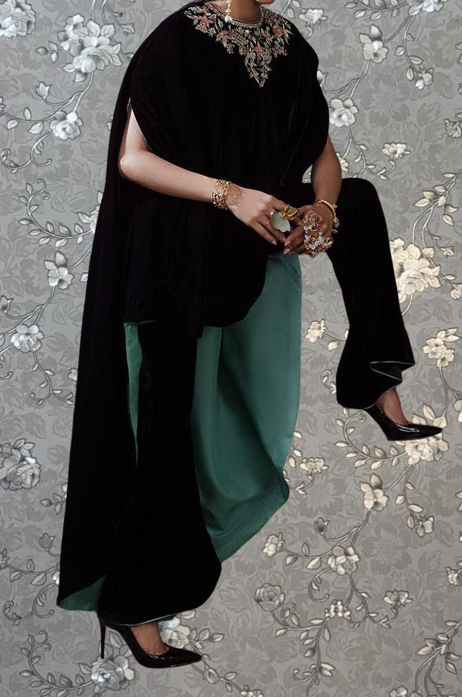 A person wearing a black cape and holding a green purse is standing against a gray floral background.