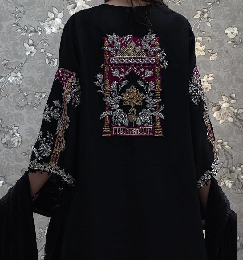 a person wearing a black dress with intricate embroidered designs on the back.