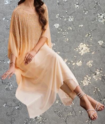 A woman wearing a peach-colored dress with a floral pattern, sitting on a chair against a gray floral background.