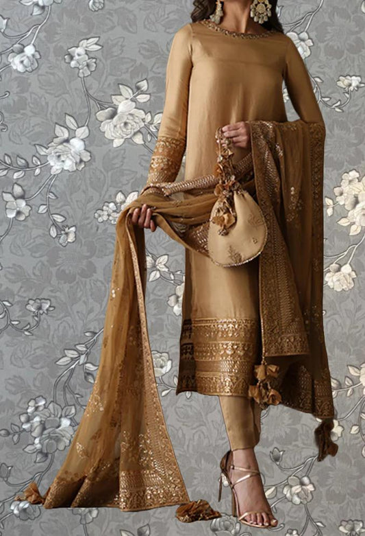 A woman wearing a gold and beige dress with a matching gold and beige shawl, standing against a gray floral background.