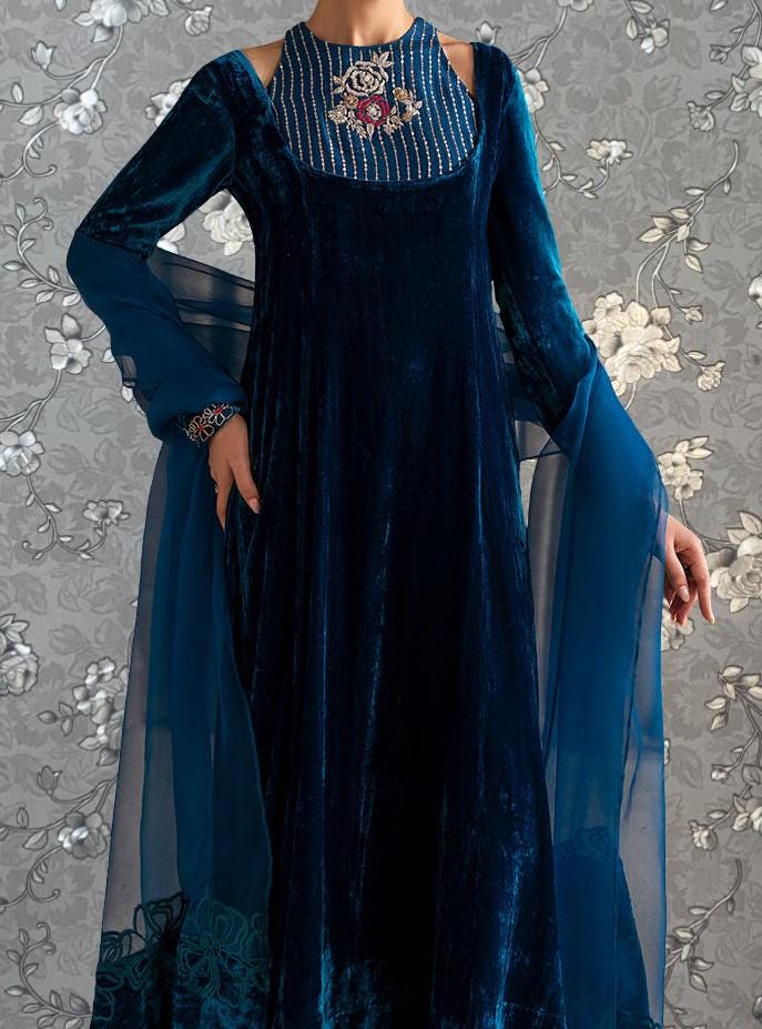 A woman wearing a long, blue velvet dress with a high neckline and a floral pattern on the skirt.