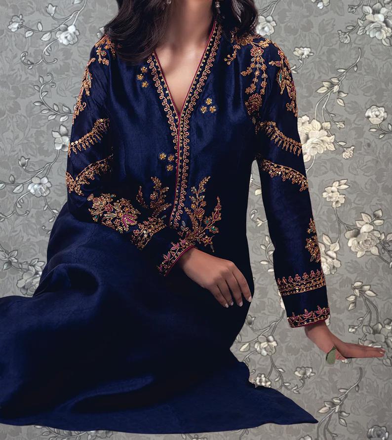 A woman wearing a blue dress with gold embroidery poses against a gray floral background.