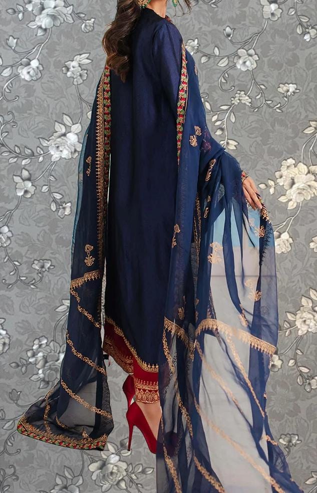 A woman wearing a navy blue dress with gold embroidery and a matching blue shawl, standing against a gray floral background.