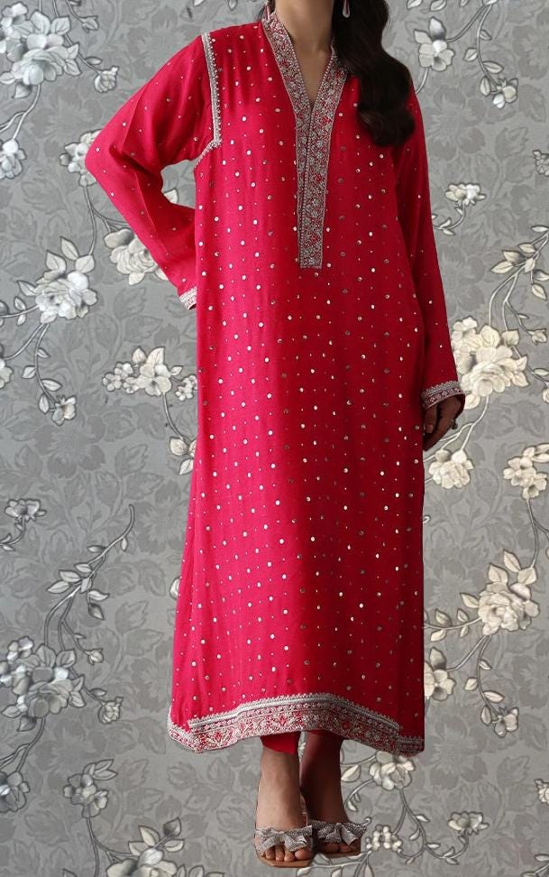 A woman wearing a long, red dress with white polka dots stands against a gray floral background.