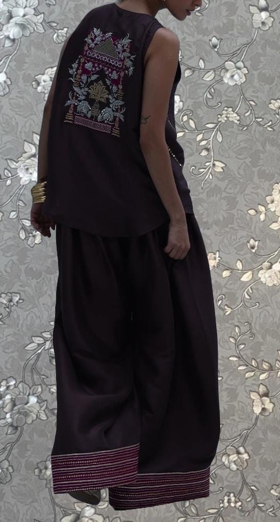 A person wearing a sleeveless top with a floral design on the back, paired with a long skirt, stands against a floral patterned background.