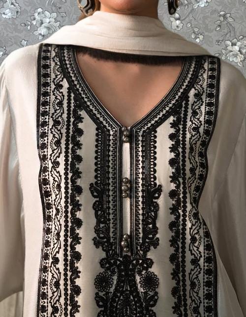 A close-up of a person wearing a white dress with black embroidered patterns and buttons.