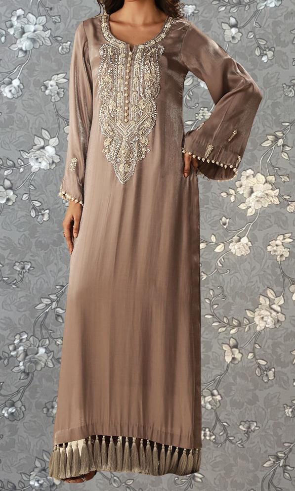 A woman wearing a long, beige dress with intricate embroidery and tassels on the bottom.