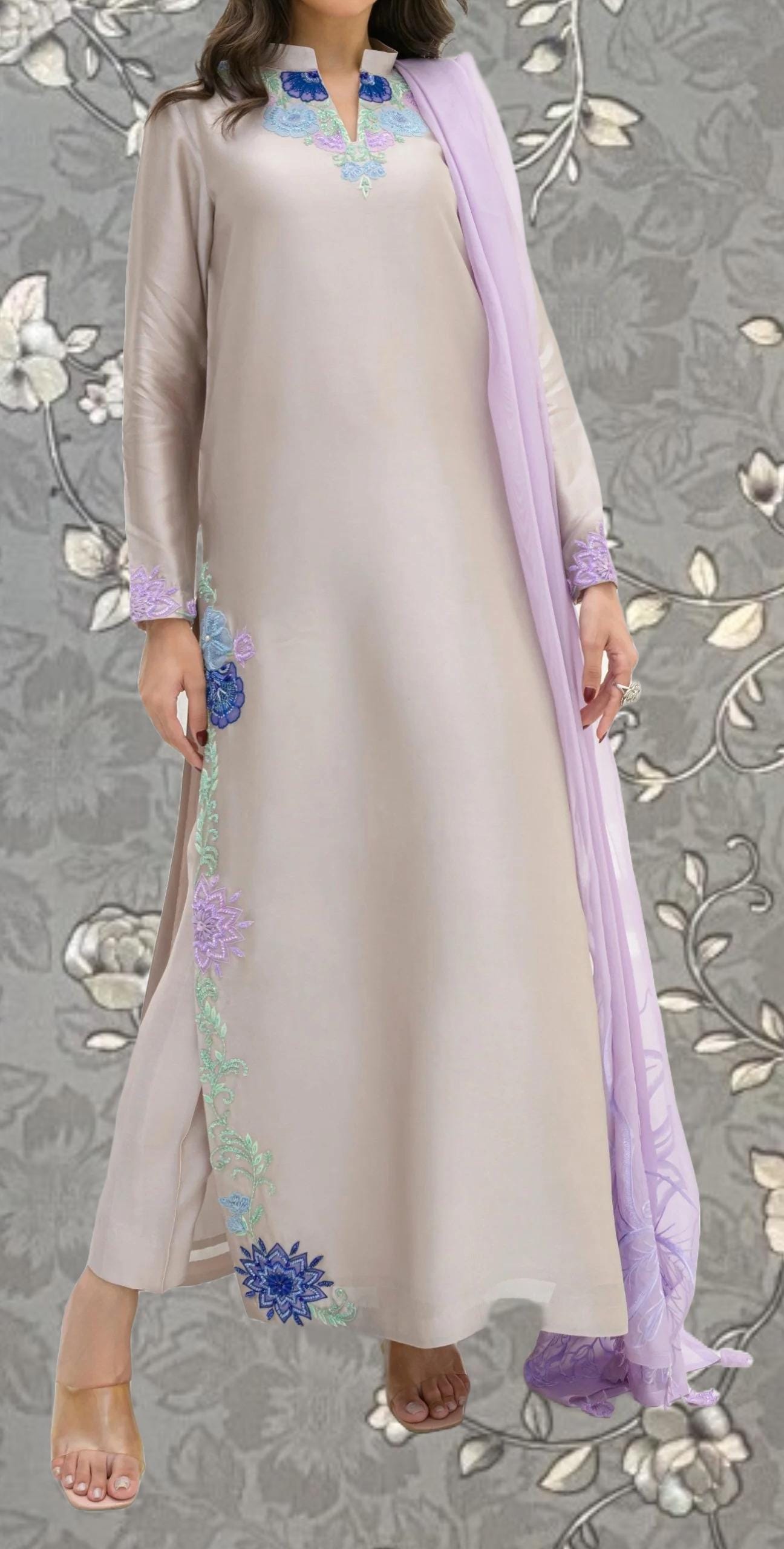 A woman wearing a long, light-colored dress with a floral pattern on the side and a matching purple shawl draped over her shoulders.