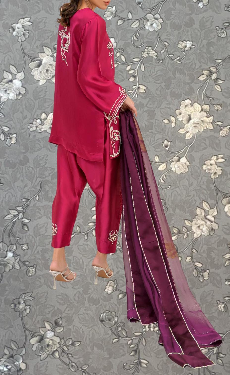 A woman wearing a red outfit with a purple shawl is standing against a gray floral background.